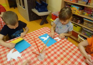 Dzieci naklejają elementy pracy na kartkę.